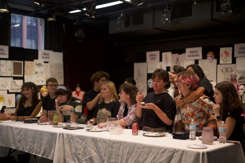 Candid photo of a group of Drama: Production & Design standing behind a long table while eating refreshments during their final project presentations.